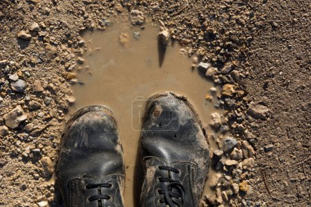 Foto de Two dirty military boots stand in a muddy puddle, suggesting a rugged environment and hard use. The boots are worn and covered in mud, adding a sense of grit and grime. The muddy water and dirty boots together create a rough and tough scene - Imagen libre de derechos