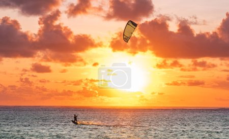 Photo for Sunset sky over the Indian Ocean bay with a kiteboarder riding kiteboard with a green bright power kite. Active sport people and beauty in Nature concept image. Le Morne beach, Mauritius - Royalty Free Image