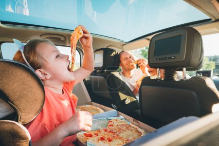 Photo for Little girl with open mouth portrait eating Italian pizza sitting in modern car with mother and father. Happy family moments, childhood, fast food eating or auto journey lunch break concept image. - Royalty Free Image