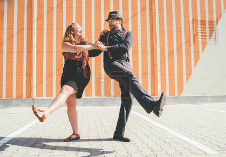 Téléchargez les photos : Couple joyeux dansant une danse swing rétro à la musique jazz qui était très populaire pendant l'ère West Coast Swing dans les années 1920-1940. Ils se sourient l'un à côté de l'autre sur fond de mur rayé. - en image libre de droit