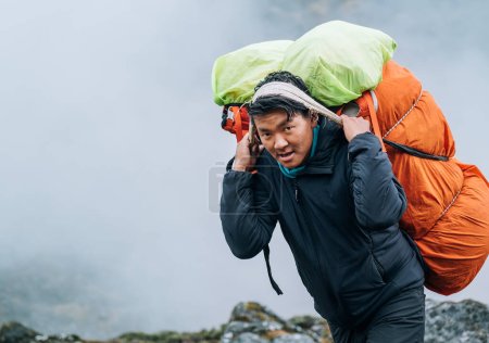 Porträt eines starken Sherpa-Mannes, der als Träger arbeitet und eine riesige Fracht mit traditioneller Methode auf der Stirn trägt. Himalaya Expedition während der Besteigung des Mera-Gipfels. Transport- oder Güterverkehrskonzept
