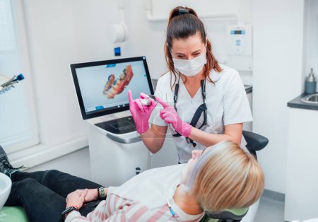 Téléchargez les photos : Dentiste femme médecin en uniforme à l'aide d'un scanner dentaire 3D intra-oral Machine pour la production d'aligneurs clairs. Le patient de la clinique dentaire visite le service médical moderne. Soins dentaires santé, concept de l'industrie de l'assurance-maladie. - en image libre de droit