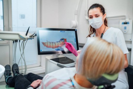 Téléchargez les photos : Dentiste femme médecin en uniforme montrant numérisation de scanner dentaire 3D intra-buccale Machine au patient. Le patient de la clinique dentaire visite le service médical moderne. Soins des dents de santé, assurance-maladie. - en image libre de droit