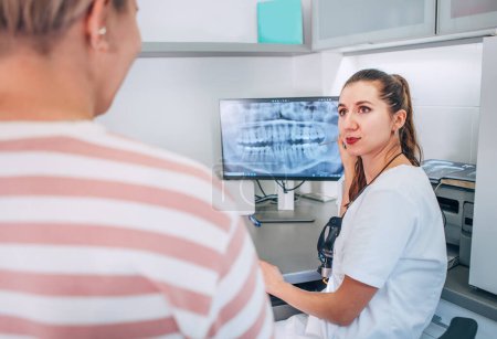 Zahnärztin in Uniform zeigt intraorale 3D-Röntgenbilder der Patientin auf dem PC-Bildschirm. Zahnklinikpatienten besuchen moderne medizinische Abteilung. Gesundheitspflege, medizinische Industrie und Technologie.