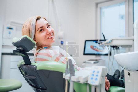 Porträt einer jungen lächelnden Frau, die nach einer zahnhygienischen Prozedur im Behandlungsstuhl der Klinik für Stomatologie sitzt und sich auf das 3D-Zähnescannen vorbereitet. Image der Gesundheitsfürsorge und der Stomatologie