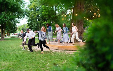 Téléchargez les photos : Soirée dansante joyeuse à l'extérieur, mettant en vedette des individus de différents âges profitant de l'ambiance festive sous des lumières lumineuses. Ils dansent swing dance dans le parc de la ville d'été - en image libre de droit