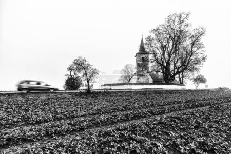 Photo for Rural country with blurred car motion and old gothic church in Ludrova village in Slovakia. Black and white photo - Royalty Free Image