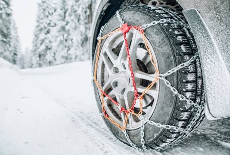 Snow chains on tire of car on snowy road in winter forest
