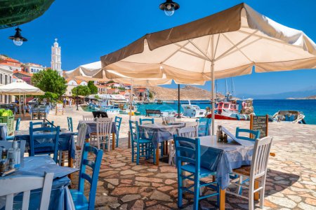 Foto de Halki, Grecia - 6 de julio de 2022: Taberna griega con vista al mar Egeo en la pequeña isla pintoresca Halki (Chalki) en Grecia - Imagen libre de derechos