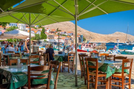 Foto de Halki, Grecia - 6 de julio de 2022: Taberna griega con vista al mar en la pequeña isla pintoresca Halki (Chalki) en Grecia - Imagen libre de derechos