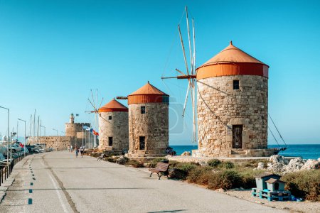Foto de RHODES, GRECIA - 4 de julio de 2022: Molinos de viento y fortaleza de San Nicolás en el puerto de Mandraki en la ciudad de Rodas. - Imagen libre de derechos