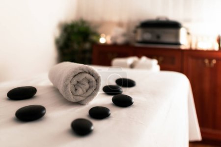 Towel and lava stones on massage table in spa salon.