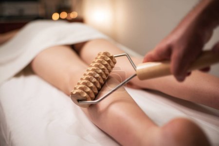 Wooden roller tool for anti cellulite massage. Massaging legs.