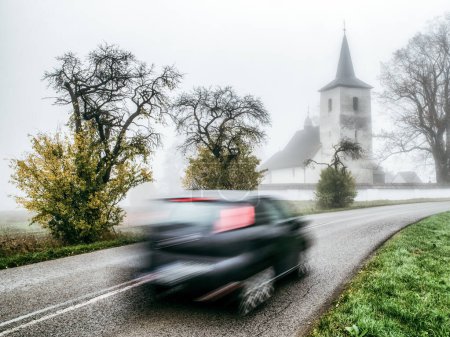 Photo for Blurred car motion on the road with old church at background. Village Ludrova in Slovakia - Royalty Free Image