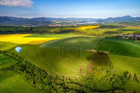 Téléchargez les photos : Liptovsky Mikulas, Slovakia - Jun 2, 2021: Blue hot-air balloon and beautiful green fields and lake Liptovska Mara under in Liptov area - en image libre de droit