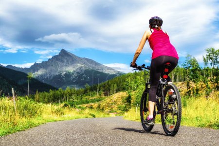 Sporty woman on MTB bike on road in Koprova valley at High Tatras mountains, Slovakia. Summer sport activity. Peak Krivan at backrouund