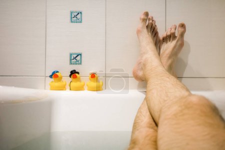 Photo for Legs of man relaxing in the bath and yellow ducks. - Royalty Free Image