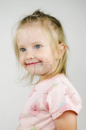 Téléchargez les photos : Petite fille avec les cheveux ébouriffés et sourire sur le visage posant en atelier avec fond - en image libre de droit