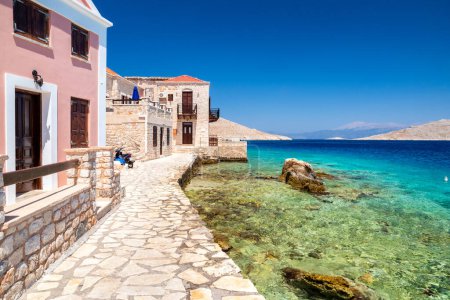 Foto de Halki, Grecia - 6 de julio de 2022: Casa de piedra y costa con mar Egeo en la isla de Halki en Grecia - Imagen libre de derechos