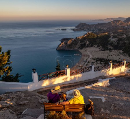 Foto de Turistas sentados en el banco en el antiguo monasterio de Panagia Tsambika y mirando el maravilloso paisaje con el mar Egeo y el país griego en la isla de Rodas en Grecia - Imagen libre de derechos