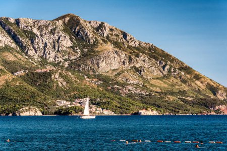 Photo for People swimming and sailboat floating on the Adriatic Sea in Montenegro. Saint Setafan Island in the background . - Royalty Free Image