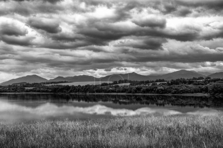 Téléchargez les photos : Reflet de nuages sombres dans l'eau avec des montagnes à l'arrière-plan. - en image libre de droit