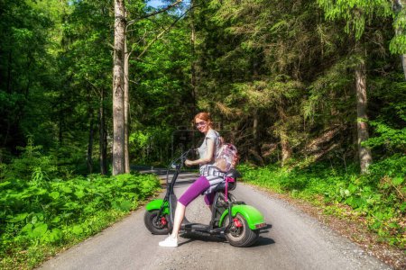 Mujer en scooter eléctrico posando en camino de asfalto en la naturaleza. Valle de Gaderska en las montañas de Great Fatra en Eslovaquia