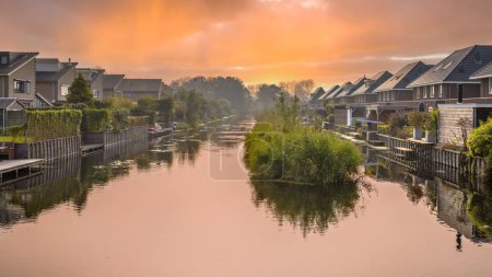 Photo for Homes on water edge in residential area in the Netherlands. Under orange sky. - Royalty Free Image