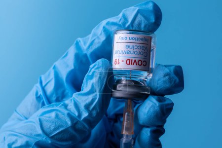 Photo for Hand with medical glove holding injection solution and syringe of Corona virus vaccine. Copy space - Royalty Free Image