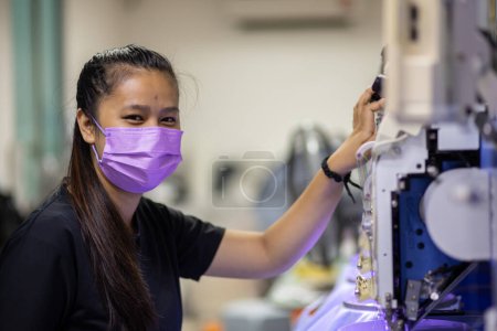 Téléchargez les photos : Une travailleuse opère une machine à broder dans l'industrie textile à la fabrication de vêtements - en image libre de droit
