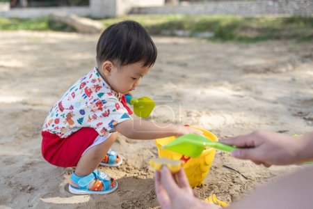 Téléchargez les photos : Un petit garçon chinois asiatique sur la plage dans les jouets pour le sable. Jeux pour enfants. Jeux sur la plage - en image libre de droit