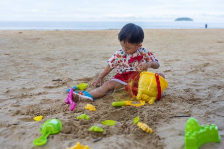Photo for An Asian Chinese baby boy on the beach in the toys for the sand. Children's games. Games on the beach - Royalty Free Image