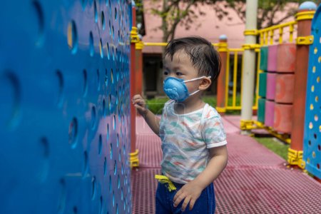 Téléchargez les photos : Asiatique enfant jouer au parc aire de jeux avec masque médical pendant la journée - en image libre de droit