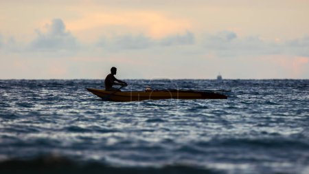 Téléchargez les photos : Silhouette Pêcheur en bateau sur la plage en fin de soirée - en image libre de droit