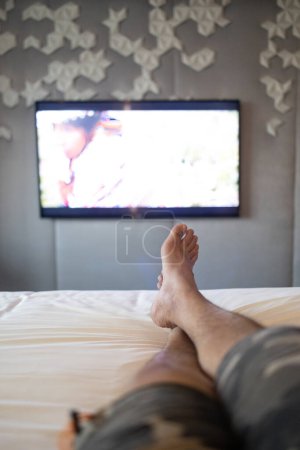 Téléchargez les photos : Jambes masculines relaxantes sur le lit d'hôtel - en image libre de droit