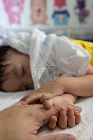 Téléchargez les photos : Un tout-petit tenant la main du père pendant le sommeil du bébé. Père prenant soin de son fils enfant heureux rêve familial de santé - en image libre de droit