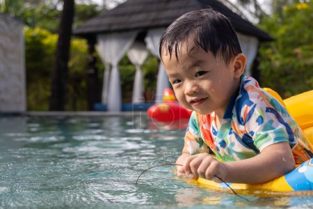 Téléchargez les photos : Un enfant asiatique heureux et appréciant jouer de l'eau sur la piscine avec anneau de natation gonflable pour enfants - en image libre de droit