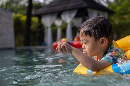 Photo for An Asian kid happy and enjoying playing water on pool with large unidentified korean word on Kids' inflatable swim ring - Royalty Free Image