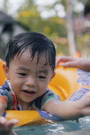 Foto de Imagen del retrato de un niño asiático feliz y disfrutando jugando al agua en la piscina con el anillo de natación inflable para niños - Imagen libre de derechos