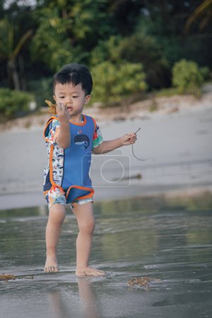 Foto de Niño chino asiático feliz jugando en la playa. El chico se divierte al aire libre. Vacaciones de verano y concepto de estilo de vida saludable - Imagen libre de derechos