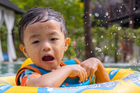 Téléchargez les photos : Portrait image d'un enfant asiatique heureux et appréciant jouer de l'eau sur la piscine avec anneau de natation gonflable pour enfants - en image libre de droit