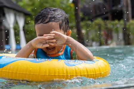 Téléchargez les photos : Un enfant asiatique heureux et appréciant jouer de l'eau sur la piscine avec anneau de natation gonflable pour enfants - en image libre de droit