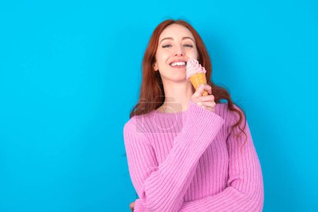 Foto de Mujer pelirroja vistiendo suéter rosa sobre fondo azul con una amplia sonrisa, muestra dientes blancos, sintiéndose seguro se alegra de tener el día libre. - Imagen libre de derechos