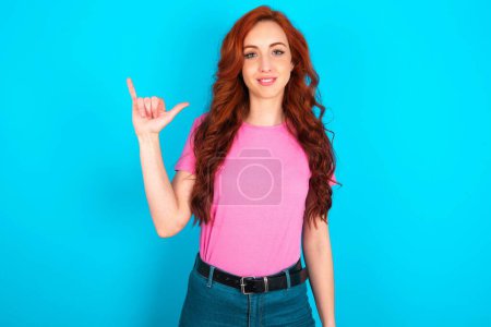 Photo for Young caucasian redhead woman wearing pink t-shirt over blue background showing up number six Liu with fingers gesture in sign Chinese language - Royalty Free Image