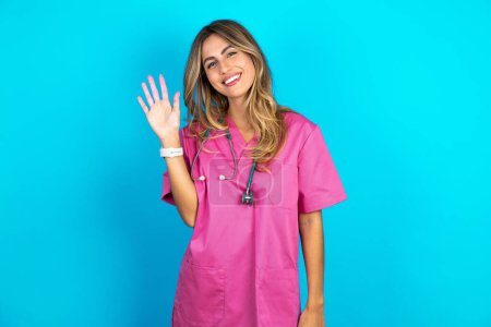 Photo for Overjoyed successful Young beautiful doctor woman standing over blue studio background raises palm and closes eyes in joy being entertained by friends - Royalty Free Image