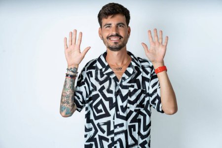 Photo for Man with tattoo wearing summer shirt standing over isolated white background showing and pointing up with fingers number ten while smiling confident and happy. - Royalty Free Image