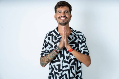 Photo for Young caucasian man wearing printed shirt praying with hands together asking for forgiveness smiling confident. - Royalty Free Image