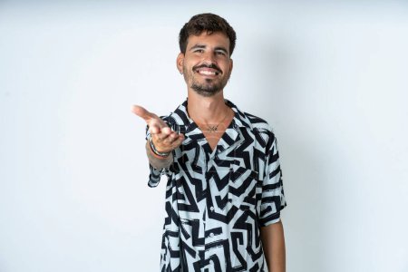 Foto de Hombre con tatuaje vistiendo camisa de verano de pie sobre fondo blanco aislado sonriendo amistoso ofreciendo apretón de manos como saludo y bienvenida. Negocios exitosos. - Imagen libre de derechos