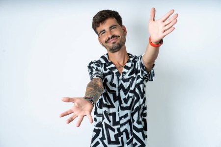 Photo for Young caucasian man wearing printed shirt looking at the camera smiling with open arms for hug. Cheerful expression embracing happiness. - Royalty Free Image