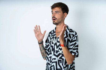 Photo for Man with tattoo wearing summer shirt standing over isolated white background shouts loud, keeps eyes opened and hands tense. - Royalty Free Image